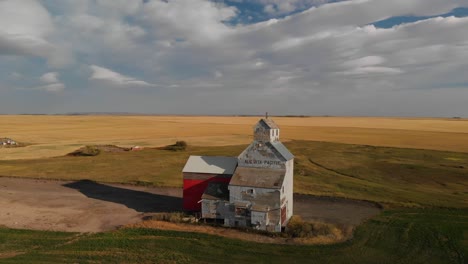 Drone-backward-shot-of-an-old-weathered-grain-elevator-for-storing-wheat-harvested-on-the-rural-area-of-Alberta,-Canada-on-a-cloudy-evening