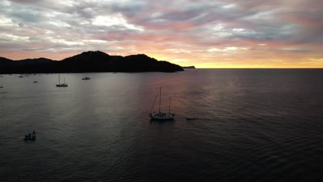 Drone-rotating-around-sailboat-navigating-at-colourful-sunset-in-Pacific-Ocean-seashore,-Costa-Rica