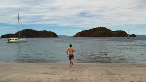 Drone-following-boy-without-t-shirt-running-towards-sea-in-Pacific-Ocean-Costa-Rican-coast