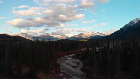 Drone-flying-over-a-turquoise-blue-water-river-into-the-wilderness-with-the-Rocky-Mountains-in-the-background-in-Nordegg,-Canada