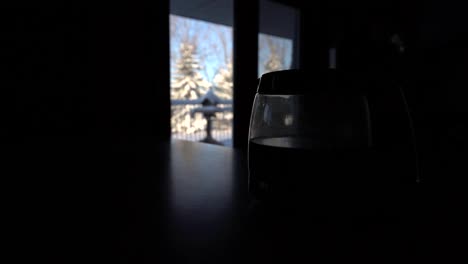 Silhouette-of-a-coffee-pot-on-a-table-in-the-living-room-with-a-winter-landscape-in-the-window