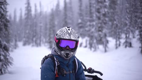Man-with-a-helmet-and-a-visor-sitting-on-a-snowmobile-and-looking-at-the-camera-in-slow-motion