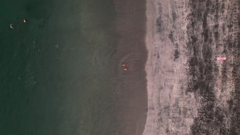Drone-ascent-revealing-two-young-girls-in-bikinis-lying-on-tropical-Costa-Rican-beach-seashore