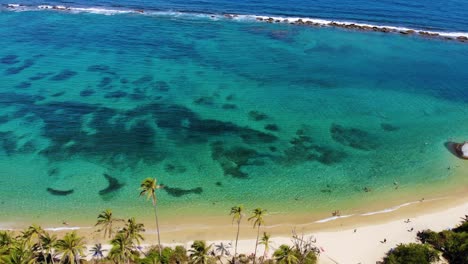 Aerial-view-overlooking-calm,-turquoise-ocean,-palm-trees-and-a-paradise-beach,-in-Tairona-national-natural-park,-serene,-sunny-evening,-in-Caribbean-Colombia,-South-America---reverse,-tilt-drone-shot