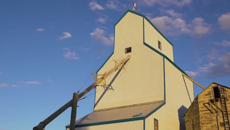 Low-angle-shot-of-a-white-grain-elevator-with-setting-sun-rays-falling-on-it-in-Alberta,-Canada-at-sunset