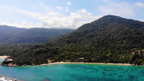 Aerial-view-of-shallow,-blue-sea,-beaches-and-rainforest-on-the-coastline-of-Tayrona,-sunny-evening,-in-Colombia---pull-back,-drone-shot