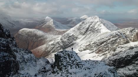 Aerial-drone-panning-shot-of-a-hiker-standing-between-the-high-Red-Cuillin-Mountains-in-winter