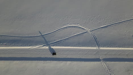 Aerial-top-down-follows-atv-vehicle-driving-along-snow-covered-road,-Casting-long-shadow