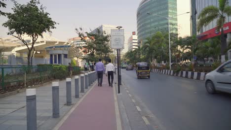 People-walking-through-the-pavements-of-smart-in-smart-city-with-emission-signage-board,-New-India-skyline-office-buildings-at-Bandra-Kurla-Complex-with-smooth-traffic-flow