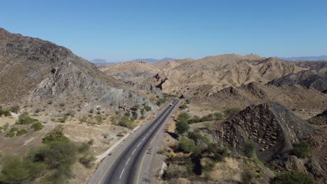 Aerial-drone-forward-moving-shot-over-truck-driving-along-winding-RCD-Road-through-mountain-range-in-Balochistan-on-a-sunny-day
