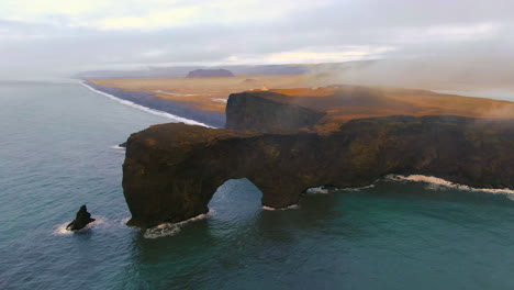 Aerial-cinematic-drone-zoom-out-circling-to-the-left-stunning-sunrise-fog-early-winter-at-Black-Sand-Beach-Apostles-fire-and-ice-ocean-next-to-Dyhrolaey-lighthouse-and-cave-Reynisfjara-Iceland
