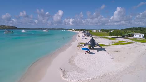 Aerial-low-pass-over-madrisqui-tropical-island,-people-enjoy-day-beach-los-Roques