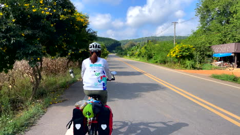A-lone-female-cyclist-rides-along-a-road-near-Paknai's-Fisherman-Village-in-the-Na-Muen-District,-Nan,-Thailand