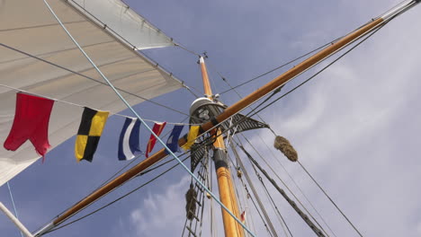 Looking-up-at-the-mast-of-a-sailboat-with-nautical-flags-blowing,-slow-motion