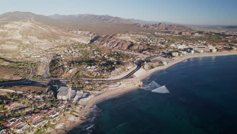 Los-Cabos-Coast,-aerial-push-in-shot-of-coastal-highway-and-resorts