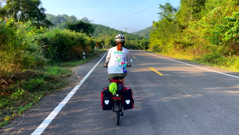 Eine-Einsame-Radfahrerin-Fährt-Eine-Straße-In-Der-Nähe-Des-Fischerdorfes-Von-Paknai-Im-Distrikt-Na-Muen,-Nan,-Thailand-Entlang
