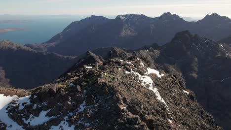 Revealing-drone-shot-of-a-hiker-enjoying-the-view-of-Cuillin-Mountain-Ridge-in-Scotland