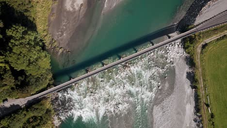 Turquoise-alpine-river-flowing-underneath-a-one-lane-bridge