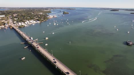 Aerial-drone-shot-on-a-sunny-day-in-Florida,-the-FPV-flying-over-the-bridge-to-the-bay-with-boats-and-yachts-anchored-in-the-shore-sea