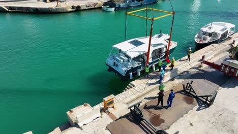 Drohnen-Luftaufnahme,-Die-Ein-In-Die-Luft-Gehobenes-Boot-Umkreist,-Während-Arbeiter-Es-Auf-Der-MMH-Werft-In-Malta-Ins-Meer-Bewegen