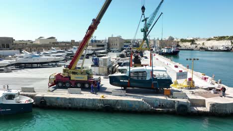 Drohnen-Luftaufnahme,-Die-Von-Einem-Boot-Wegfliegt,-Das-In-Die-Luft-Gehoben-Wird,-Während-Es-Auf-Der-MMH-Werft-In-Malta-Ins-Meer-Bewegt-Wird