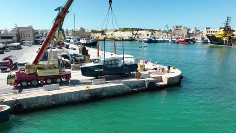 Toma-Aérea-De-Un-Dron-Que-Orbita-Lentamente-Alrededor-De-Un-Barco-Levantado-En-El-Aire-Mientras-Lo-Mueve-Hacia-El-Mar-En-El-Astillero-Mmh-Malta