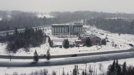 Flying-Towards-Hotel-And-Restaurant-Buildings-Amidst-Snowfall-In-Winter-In-Huntsville,-Ontario,-Canada