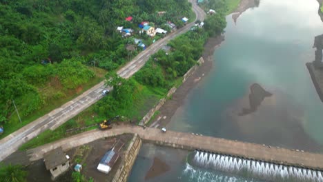 Cinematic-tilt-up-aerial-reveal-of-quaint-riverside-village-community-with-lush-jungles-and-winding-roads-in-Catanduanes,-Philippines