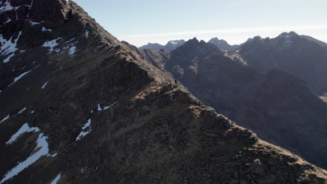 Backwards-drone-panning-shot-of-a-male-standing-at-Cuillin-Mountains-in-Scotland-on-a-sunny-day