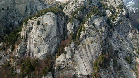 Aerial-pullback-view-of-a-rugged-mountain-and-boulders-covered-in-pine-trees-in-Val-di-Mello,-Italy
