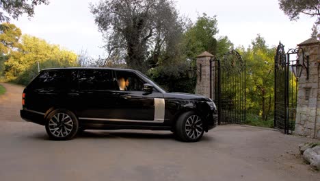 a-big-black-luxury-car-of-the-range-rover-brand-waiting-in-front-of-a-black-metal-gate,-the-gate-opens-and-the-car-enters-a-luxurious-domain