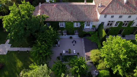 drone-shot-of-the-sky-view-of-a-large-house-in-the-south-of-france-with-ivy-on-some-facades,-a-large-building-and-a-large-wooded-area-around