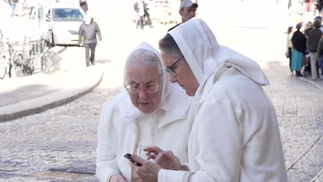 Un-Par-De-Monjas-Ancianas-Hojeando-Su-Móvil-Cerca-De-Un-Muro-De-Las-Lamentaciones