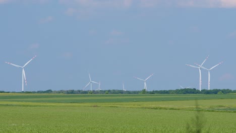 Wind-park-with-many-turbines-producing-clean-energy-in-remote-farmland,-blue-sky