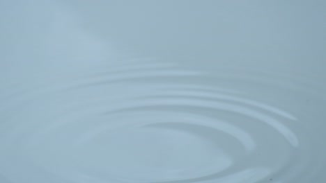 Wassertropfen-Fallen-Auf-Saubere,-Ebene-Wasseroberflächen-Und-Bilden-Kreisförmige-Wellen