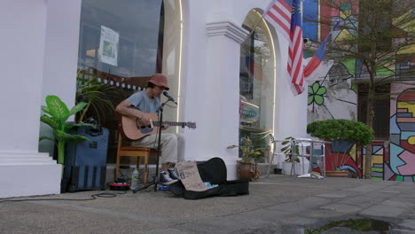Melodisches-Gitarrenspiel-Eines-Straßenkünstlers-In-Hut-In-Der-Nähe-Des-Malakka-Flusses