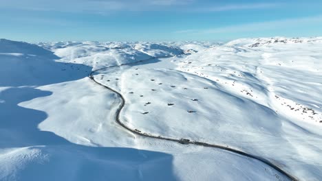 Huts-and-snow-covered-mountain-landscape-with-road-RV-13-crossing-Vikafjellet-in-western-Norway---Sunny-day-aerial