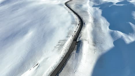 Car-crossing-snow-covered-Vikafjell-mountain-crossing-in-Norway---Beautiful-top-down-aerial-in-sunny-weather