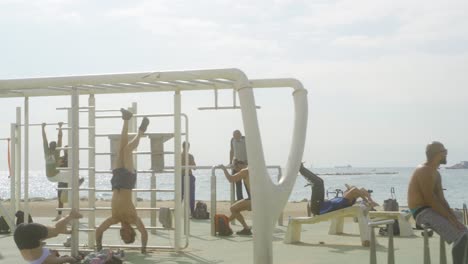 Fit-athletic-men-working-out-at-outdoor-gym-muscle-park,-Barceloneta-Beach,-Barcelona,-Spain