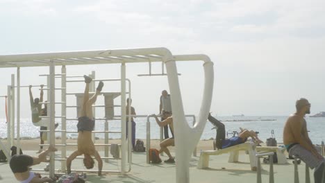 Colocar-Hombres-Atléticos-Trabajando-En-El-Gimnasio-Al-Aire-Libre-Muscle-Park,-La-Playa-De-La-Barceloneta,-Barcelona,-España