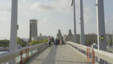 People-walking-over-bridge-Rambla-de-Mar-in-Barcelona,-Spain-on-sunny-day