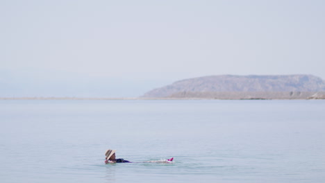 Eine-ältere-Touristin-Mit-Hut-Schwimmt-Auf-Dem-Rücken-Im-Toten-Meer-–-Israel-Und-Genießt-Beinbewegungen