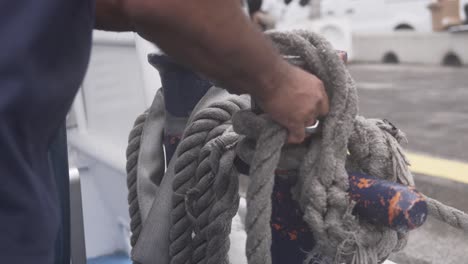 Close-up-of-a-sailor-person-tying-the-thick-rope-to-the-ship-at-the-port