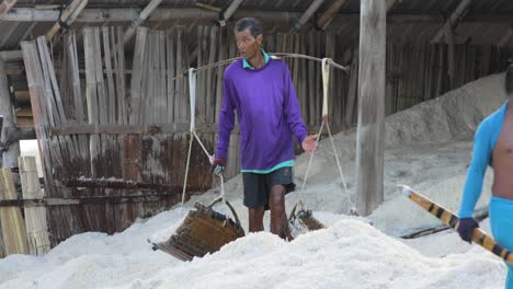 Farmer-Collecting-Sea-Salt-with-Wooden-Scoop-Empties-onto-a-Pile-for-Collection-Thailand