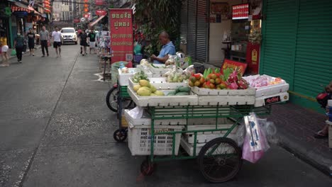 Scene-of-people-walking-and-fruit-vendors-await-customers-at-the-famous-Yaowarat-Chinatown,-Bangkok,-Thailand