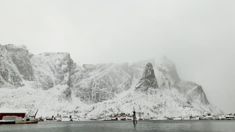 Moody-aerial-near-harbor-with-white-snowy-mountain-background,-Reine,-Lofoten
