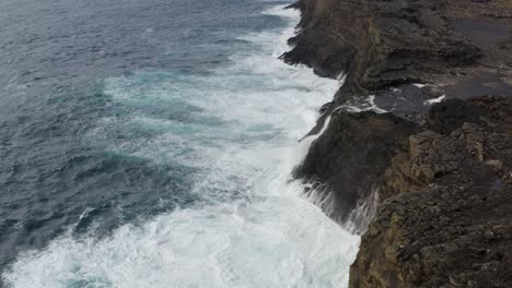 Aerial-birds-eye-Shot-of-crashing-Waves-against-rocky-coastline-of-Vagar-Island-With-Bösdalafossur-waterfall