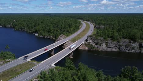 Rising-aerial-shot-of-curved-highway-bridge-over-lake-through-rock-and-trees-near-Gravenhurst-Ontario
