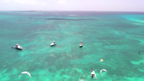 Aerial-shot-caribbean-beach-people-kitesurf-near-coast-on-turquoise-sea-water,-tilt-up
