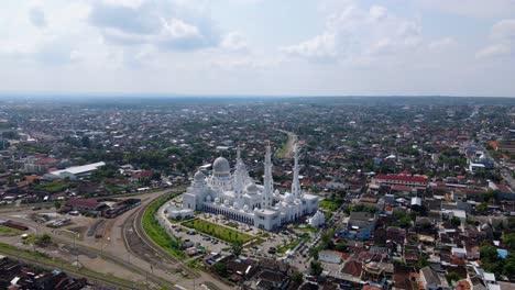 Aerial-approaching-shot-of-famous-SHEIKH-ZAYED-GRAND-MOSQUE-in-Indonesia-during-sunny-day---Cityscape-of-Solo-in-background